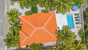 Vue aérienne d’un hôtel doté d’un grand toit orange, d’une piscine et de plusieurs palmiers.
