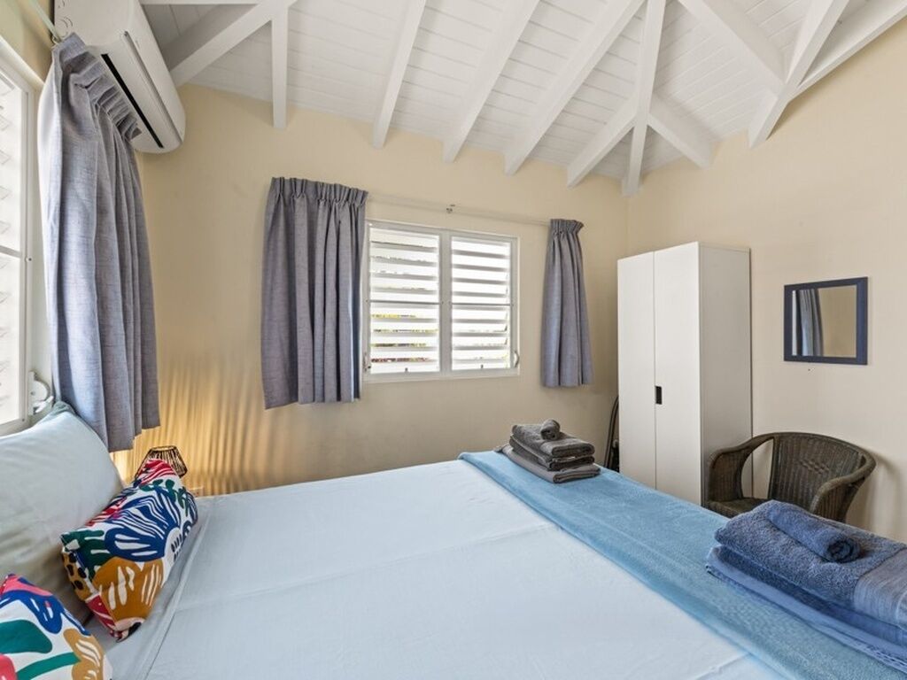 Una habitación de hotel con cama, armario, silla y ventana con cortinas.