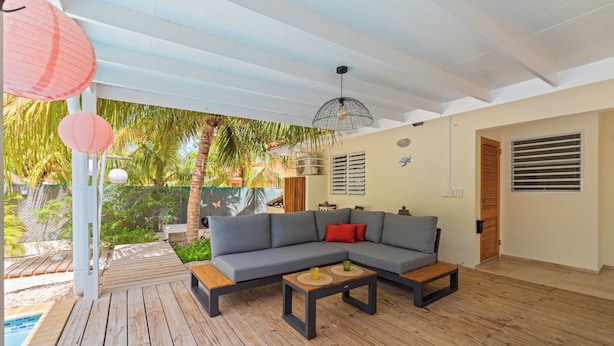 Un espace de vie moderne avec un canapé d’angle, un plancher en bois et une vue sur la piscine.