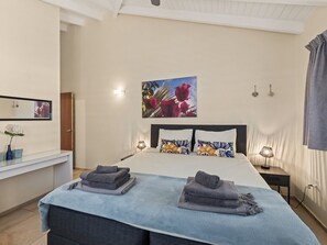 A bedroom with a bed, bedside lamps, a painting, and a mirror.