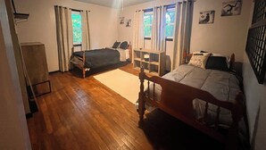 Une chambre avec deux lits, un plancher en bois, un ventilateur de plafond et une fenêtre avec des rideaux.