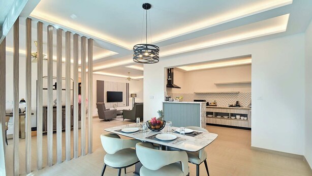 Un comedor moderno con una mesa dispuesta para cuatro, una cocina al fondo e iluminación empotrada en el techo.