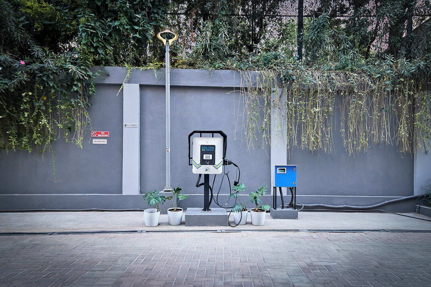 A parking area with electric vehicle charging stations, a trash bin, and potted plants.