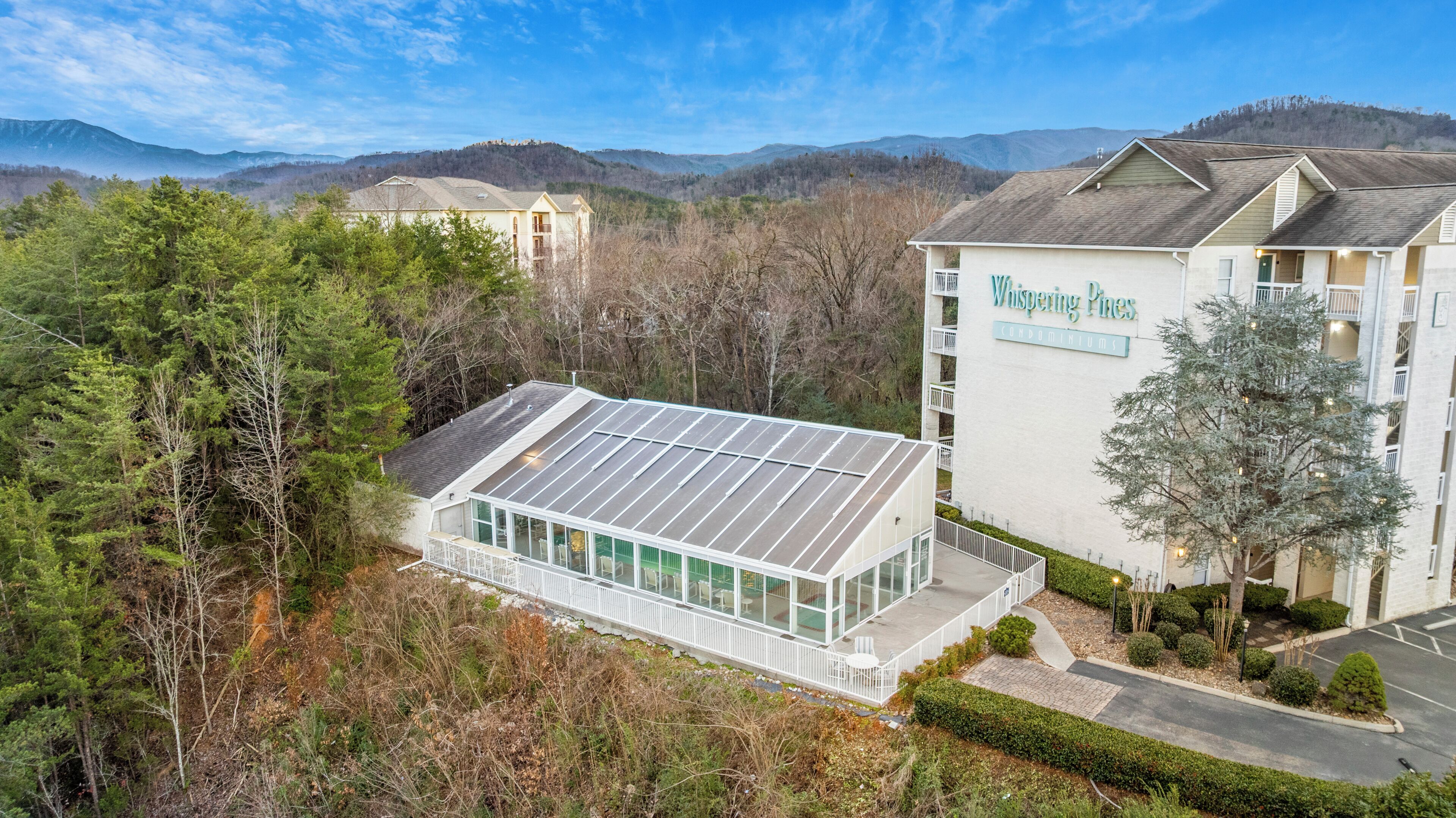 A modern building with a large glass facade and solar panels, surrounded by dense forest and mountains.