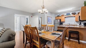 Un coin repas avec une table et des chaises en bois, un lustre et une cuisine en arrière-plan.