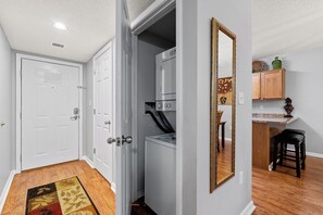 Una cocina compacta con lavadora y secadora integradas, un armario de madera y un espejo en la pared.