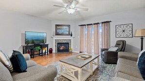 Un salon doté d’une cheminée, d’un ventilateur de plafond, d’un téléviseur et d’un coin salon confortable.