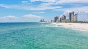 Une plage à l’eau turquoise et limpide, une rive sablonneuse et, en arrière-plan, le profil d’une ville avec ses grands immeubles.