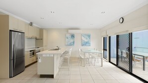 A modern kitchen with a central island, stainless steel appliances, and a dining area with white chairs. - El Penguini in Cowes (Cowes)