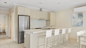 A modern kitchen with a stainless steel refrigerator, a built-in oven, and a bar area with white bar stools. - El Penguini in Cowes (Cowes)