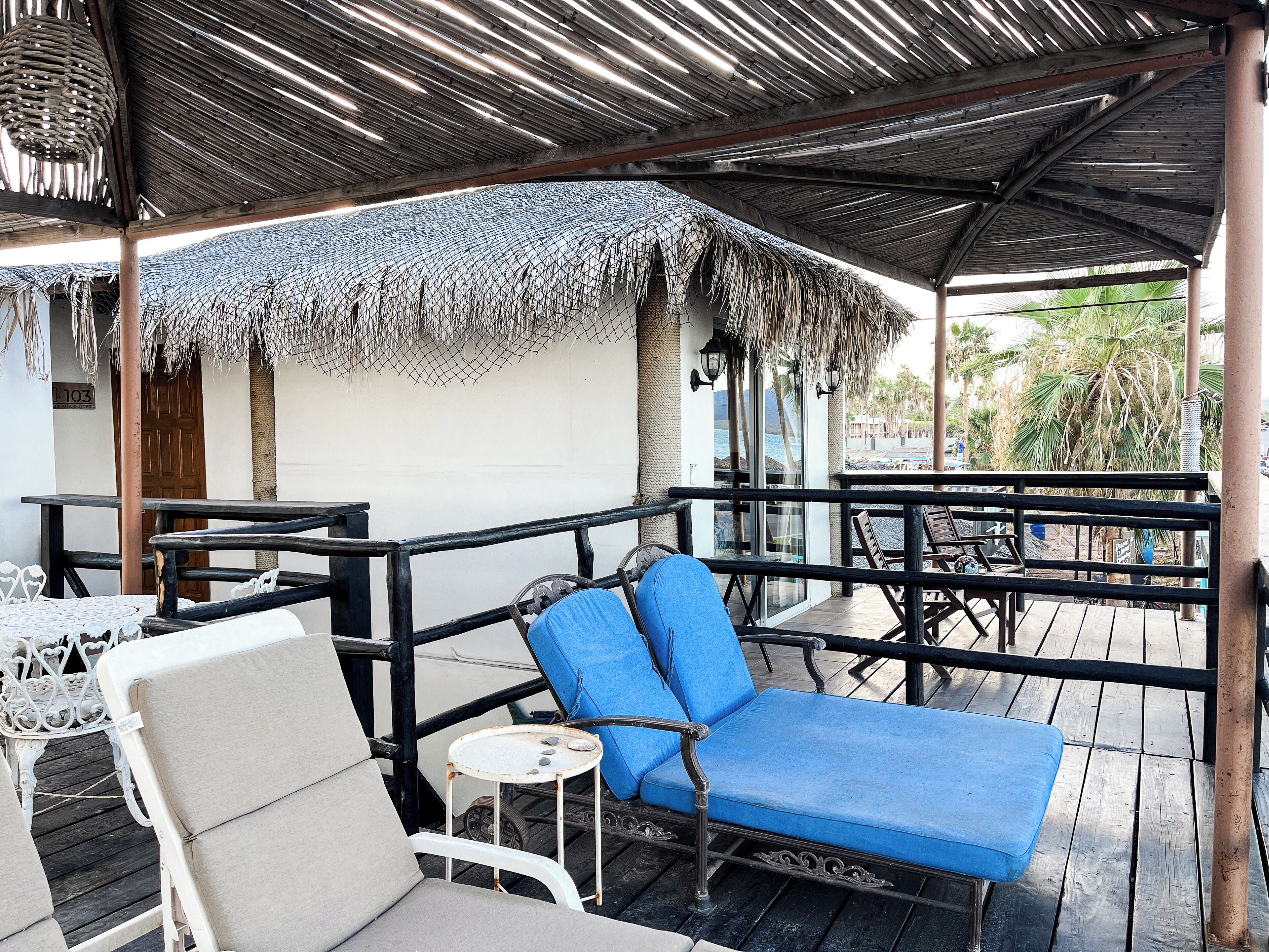 A covered outdoor seating area with a thatched roof, a wooden deck, and a view of the ocean.