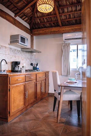 A kitchen with wooden cabinets, a microwave, a coffee maker, and a dining area with a table and chairs. - BAJA MIA SUITES AND TOURS (Loreto)