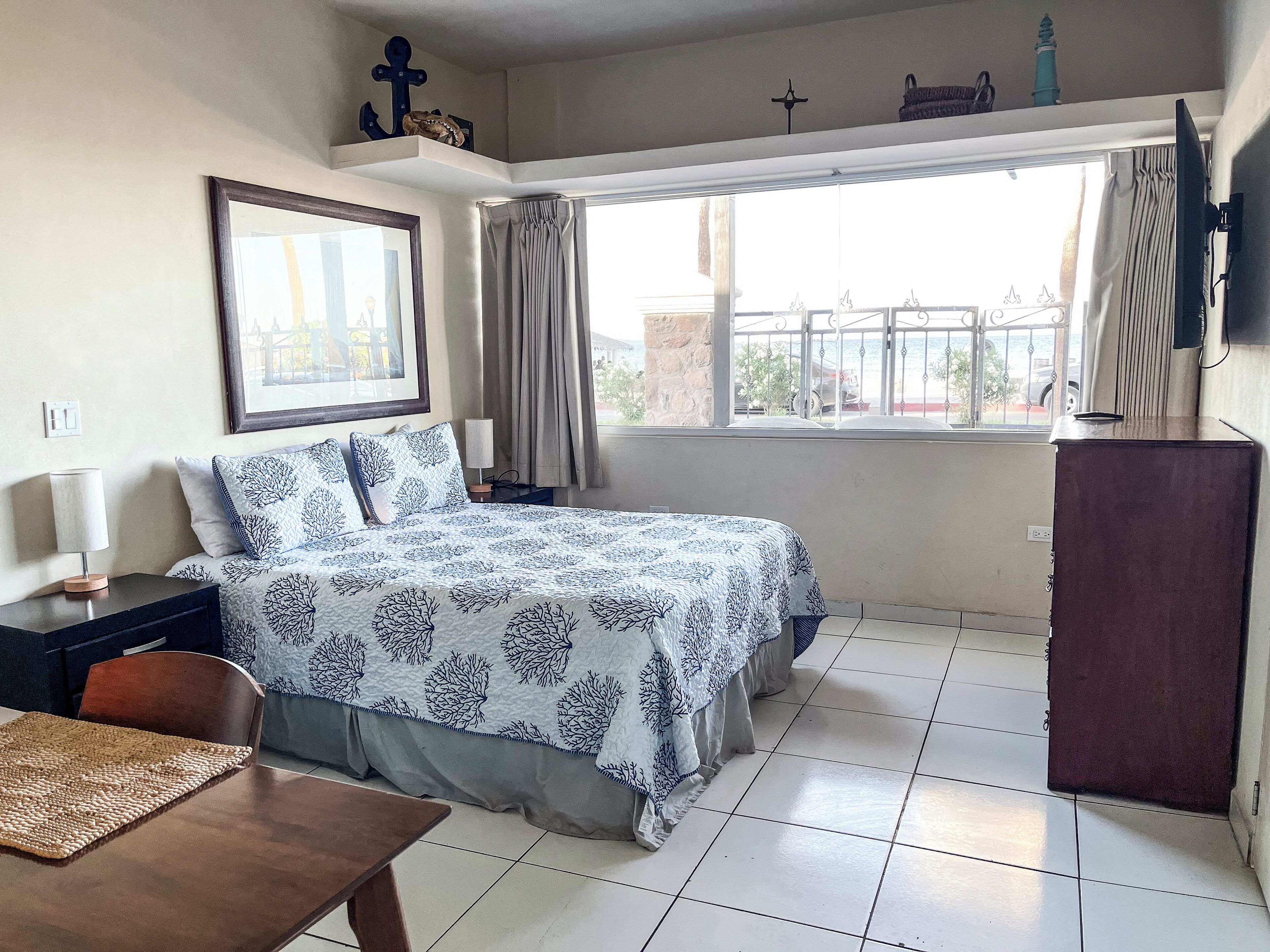 Un dormitorio con cama, escritorio, silla, televisor y ventana con cortinas.