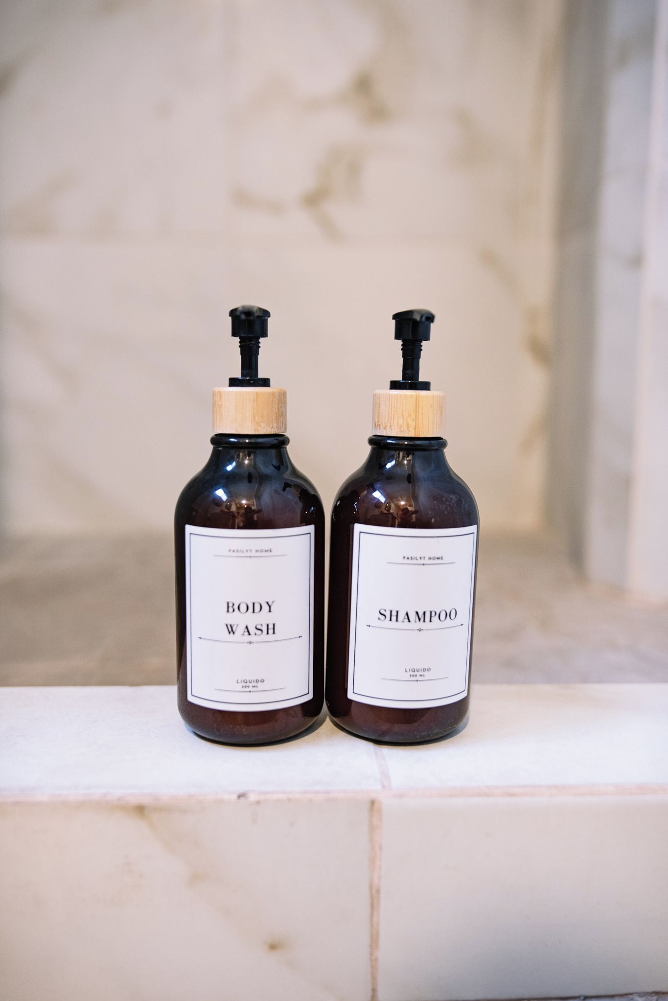 Two bottles of body wash and shampoo on a marble ledge.