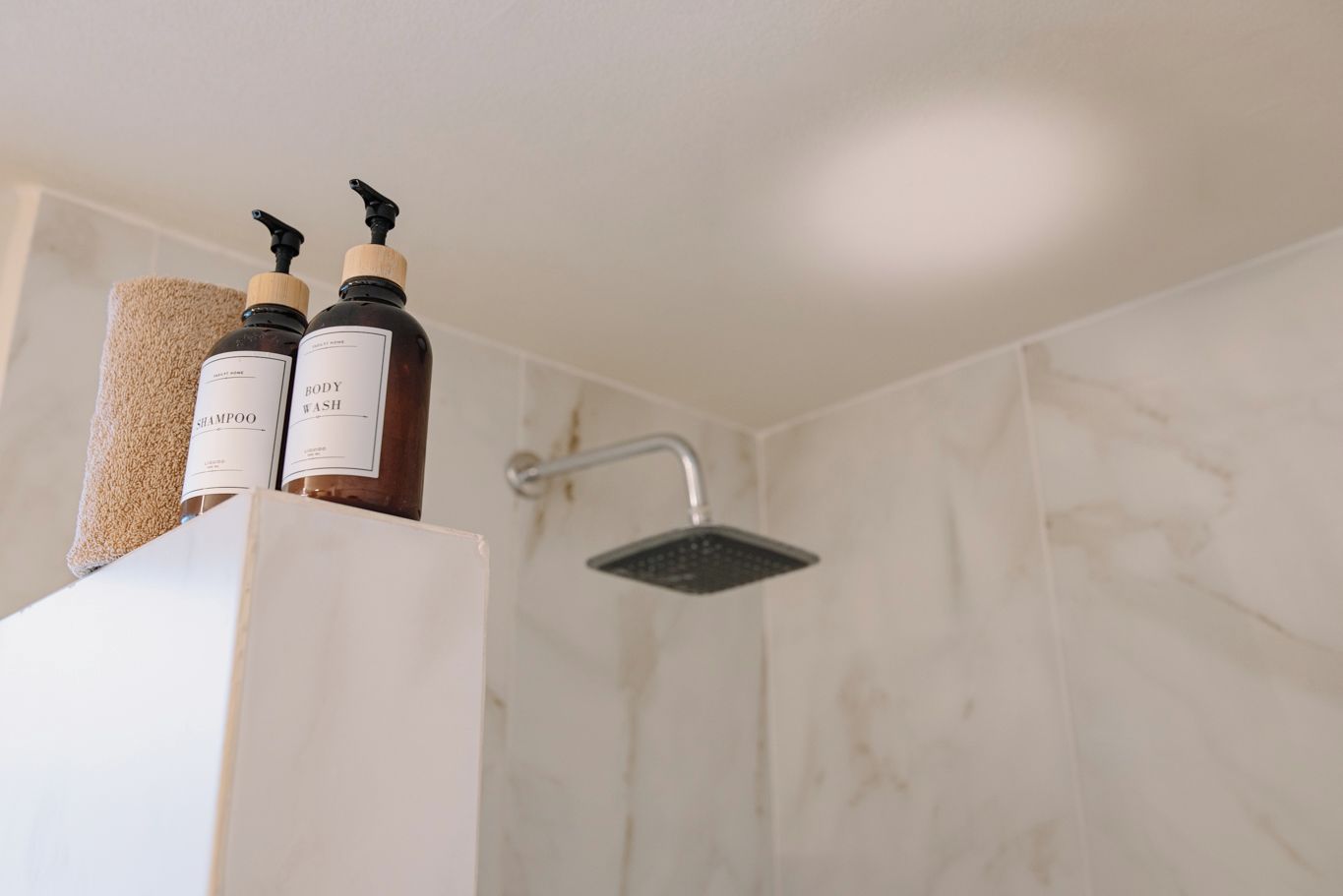 A bathroom with a shower, a towel, and two bottles of shampoo and body wash on a shelf.