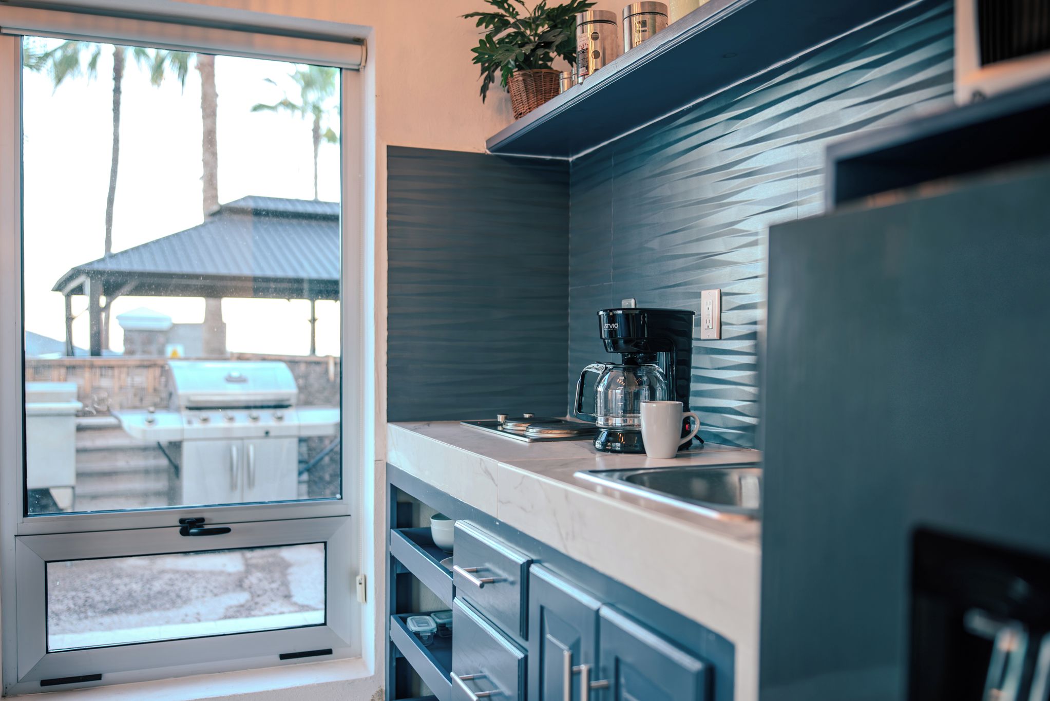 Una cocina moderna con cafetera integrada, ventana con vistas a un patio y palmeras.