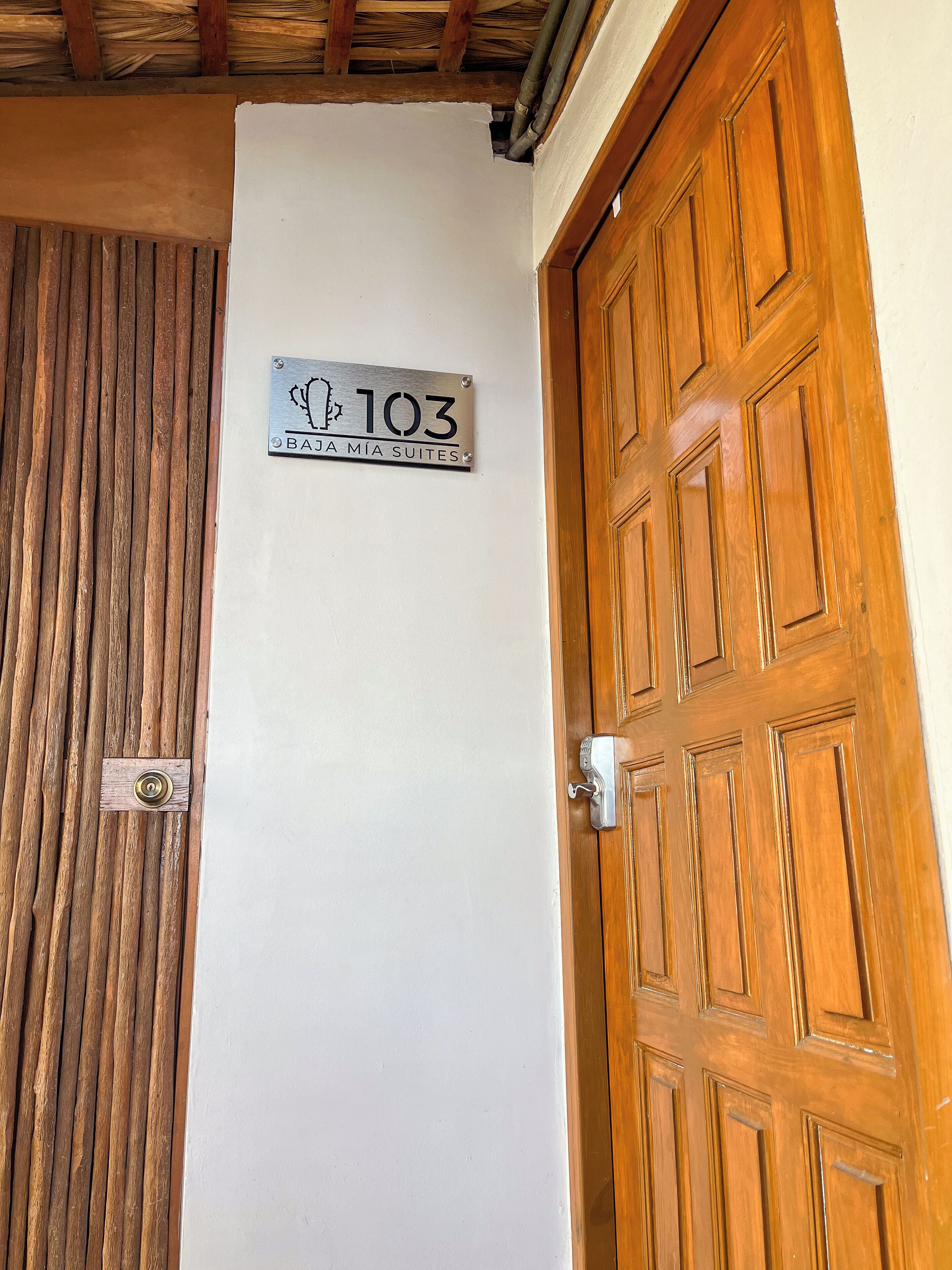 Eine Holztür mit Messingklinke und einem darüber angebrachten Schild mit der Aufschrift '103 BAZA MIA SUITES'.