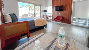 Une chambre d’hôtel équipée d’un lit, d’un bureau, d’une chaise, d’une télévision et d’une fenêtre donnant sur des palmiers.