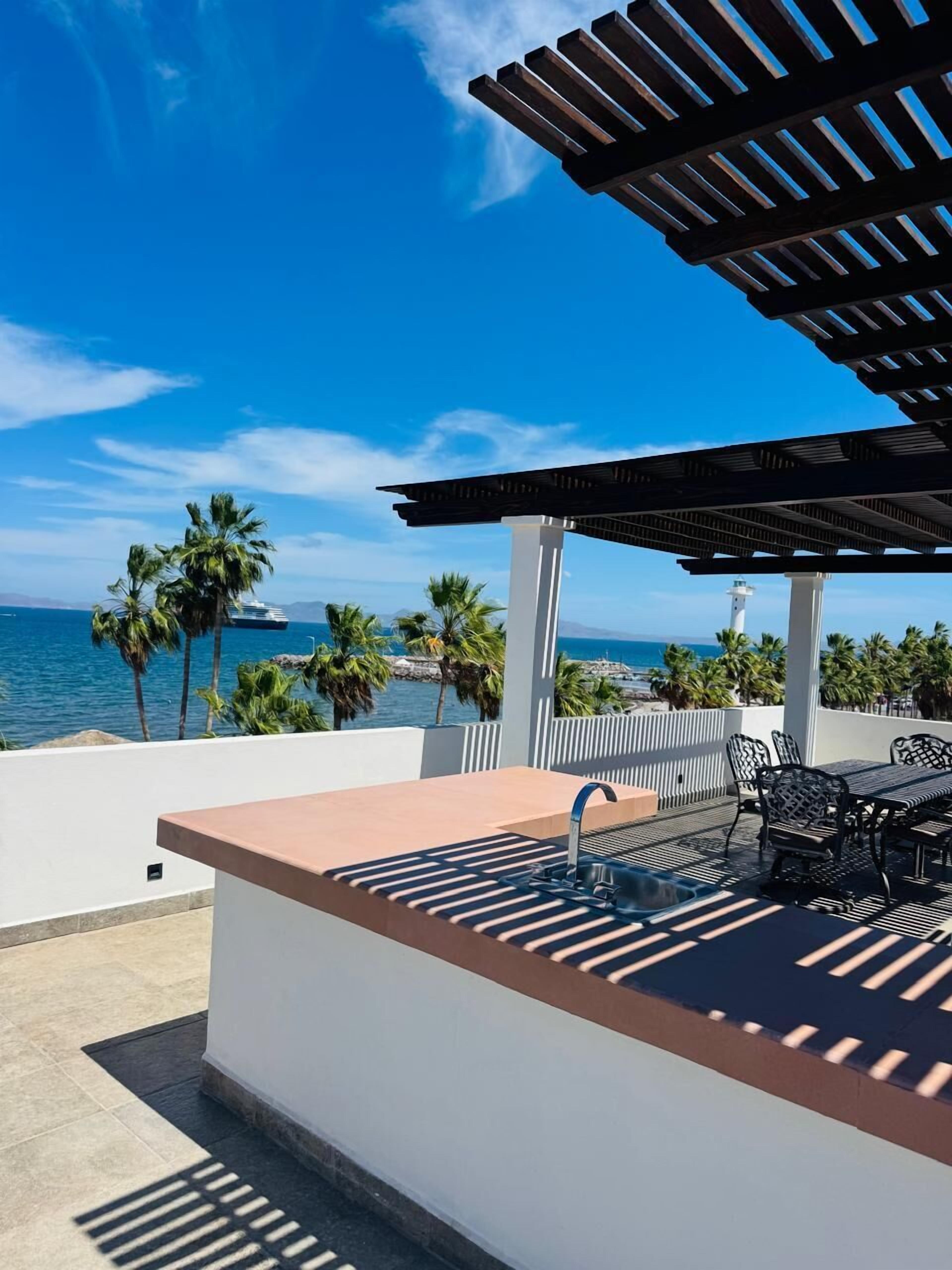 A rooftop terrace with a pool table, chairs, and a view of the ocean and a lighthouse.