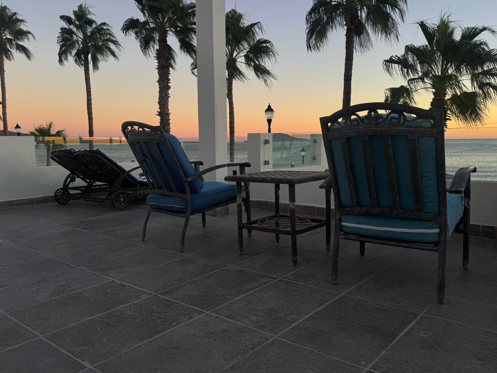Una terrazza con due sedie e un tavolo, vista su uno specchio d'acqua sullo sfondo con palme.