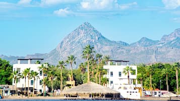 A coastal hotel with modern architecture, palm trees, and a mountain in the background.