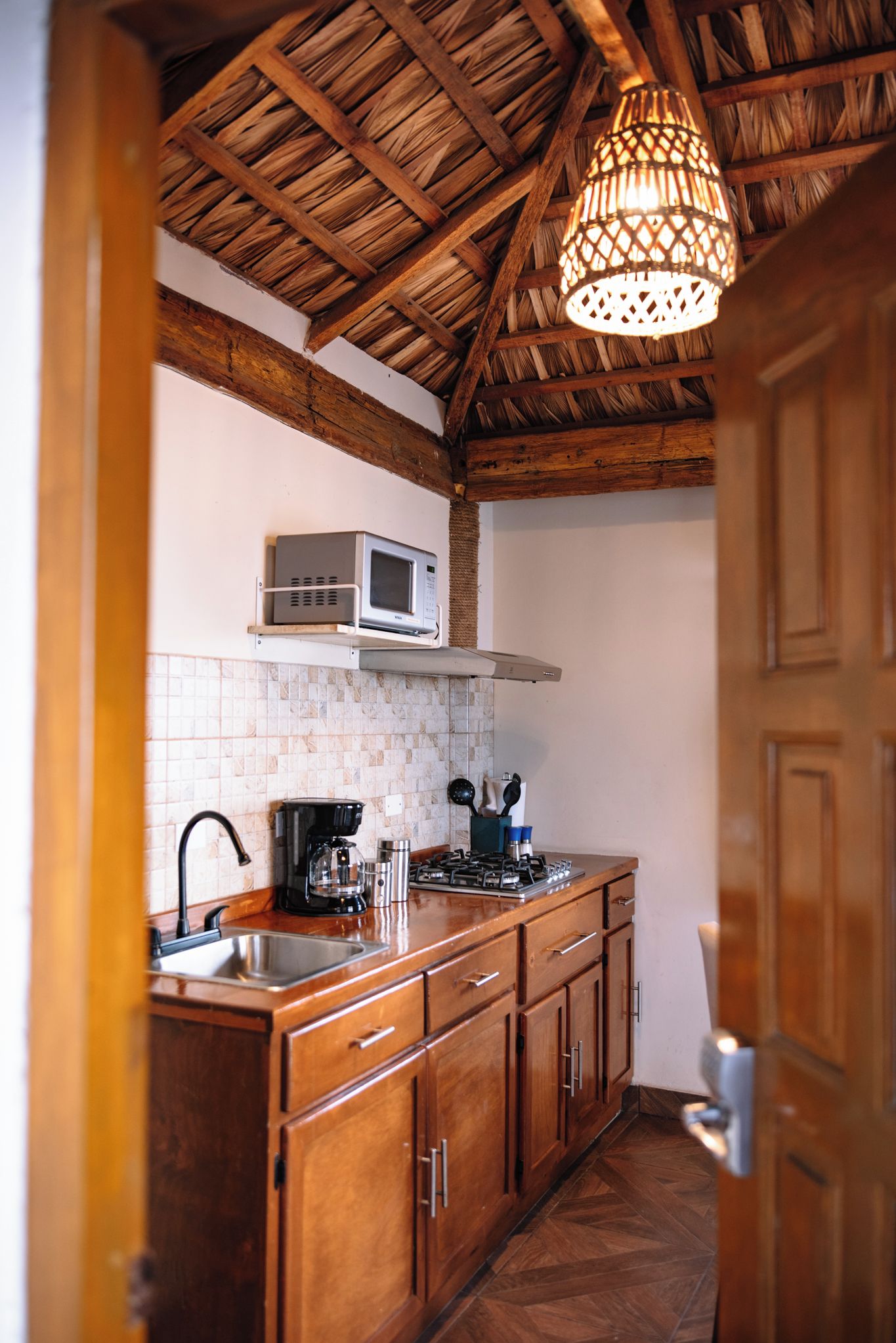 A kitchen with wooden cabinets, a microwave, a coffee maker, and a hanging light fixture.