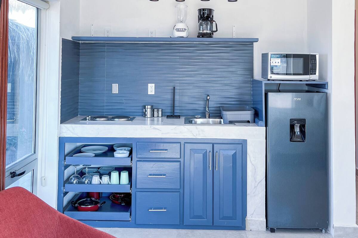 Una cocina moderna con armarios azules, microondas integrado, refrigerador y lámparas colgantes.