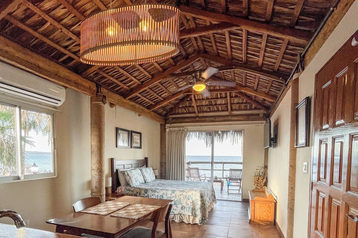 Amplia habitación con cama, comedor y cocina. Un gran ventanal ofrece vistas al océano.