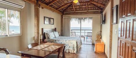 A spacious room with a bed, a dining area, and a kitchen. There is a large window providing a view of the ocean.