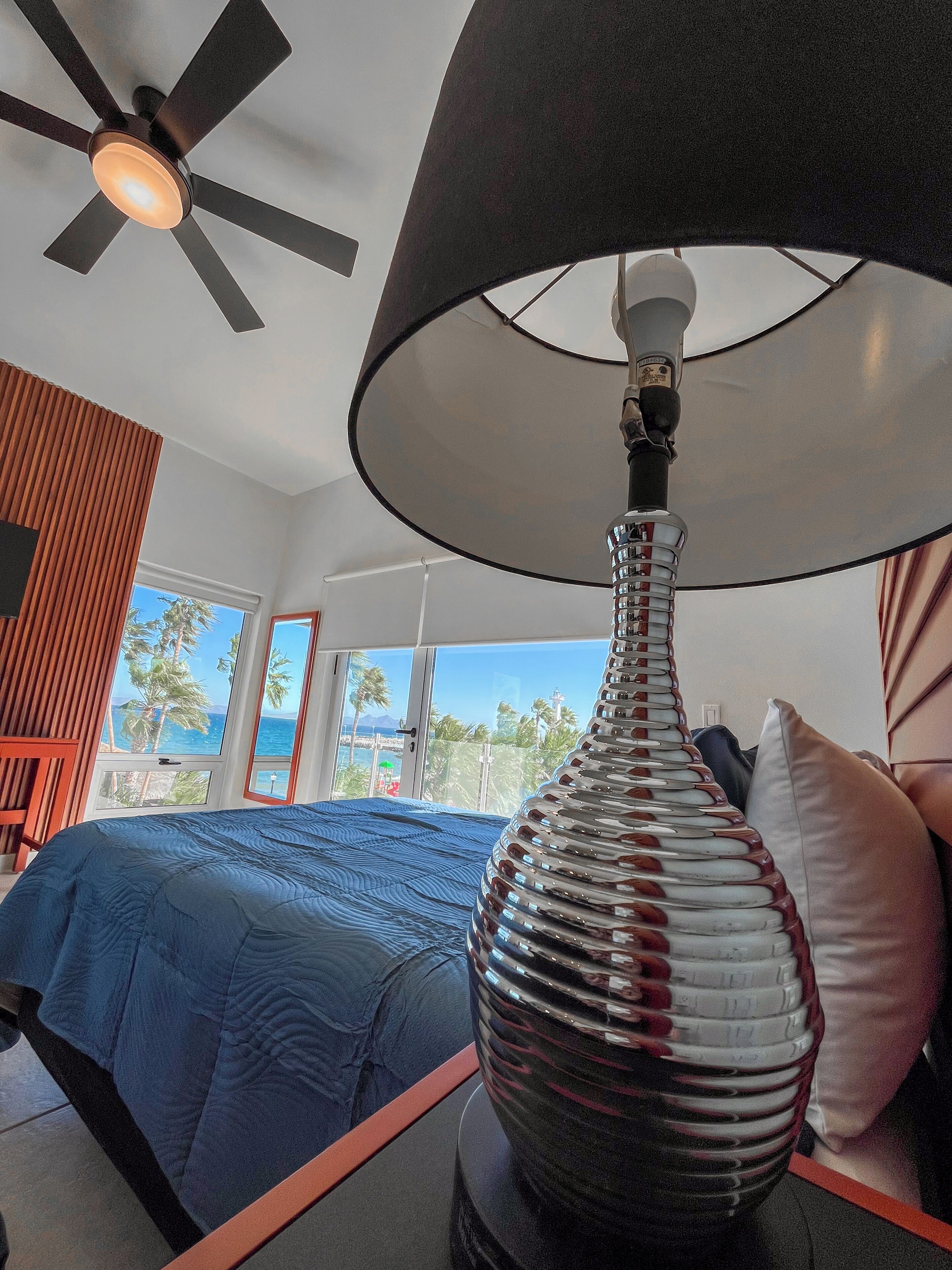 Een slaapkamer met een bed, een lamp, een plafondventilator en uitzicht op de oceaan.