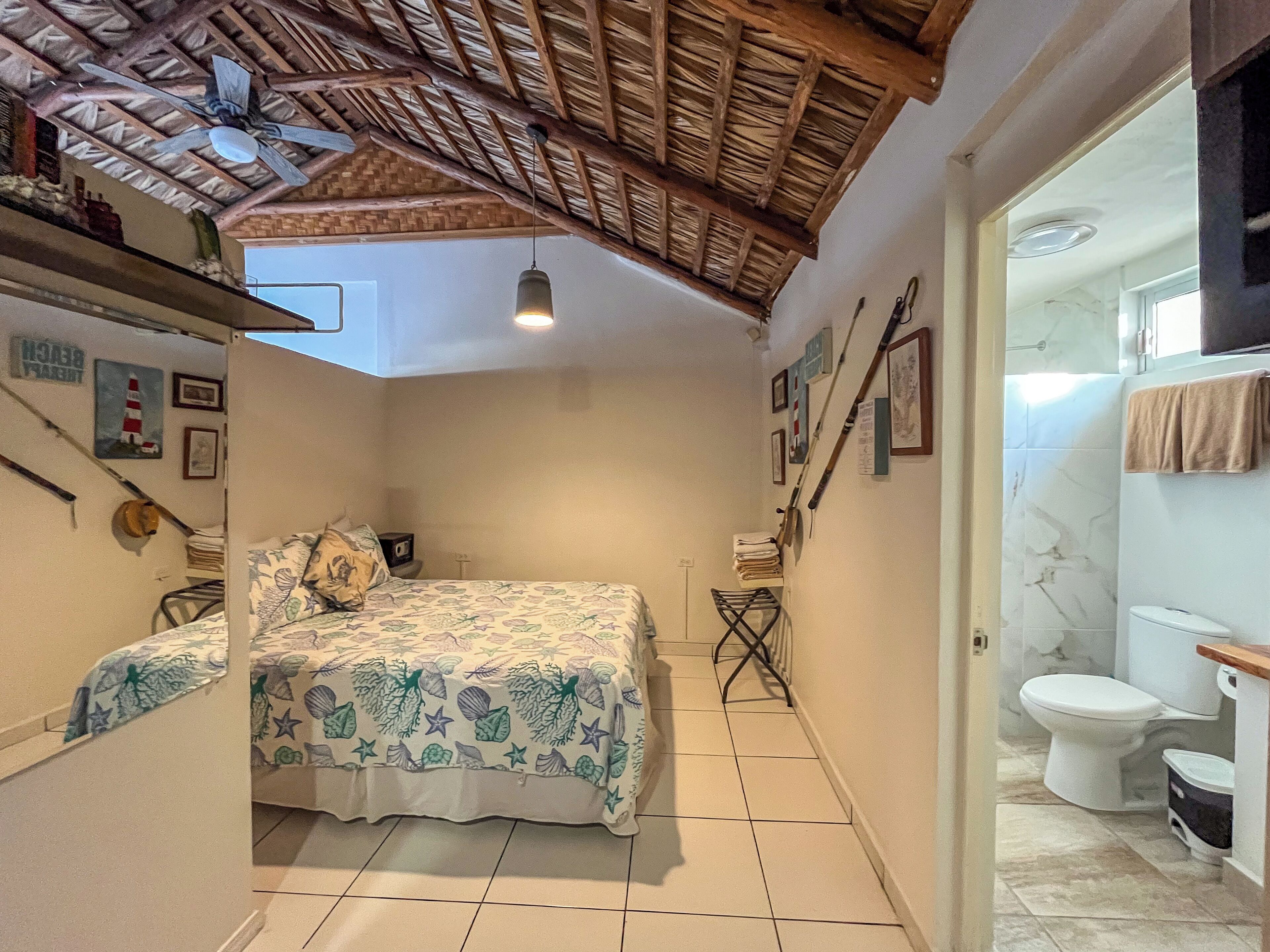 A bedroom with a bed, a ceiling fan, and a bathroom with a toilet and sink.
