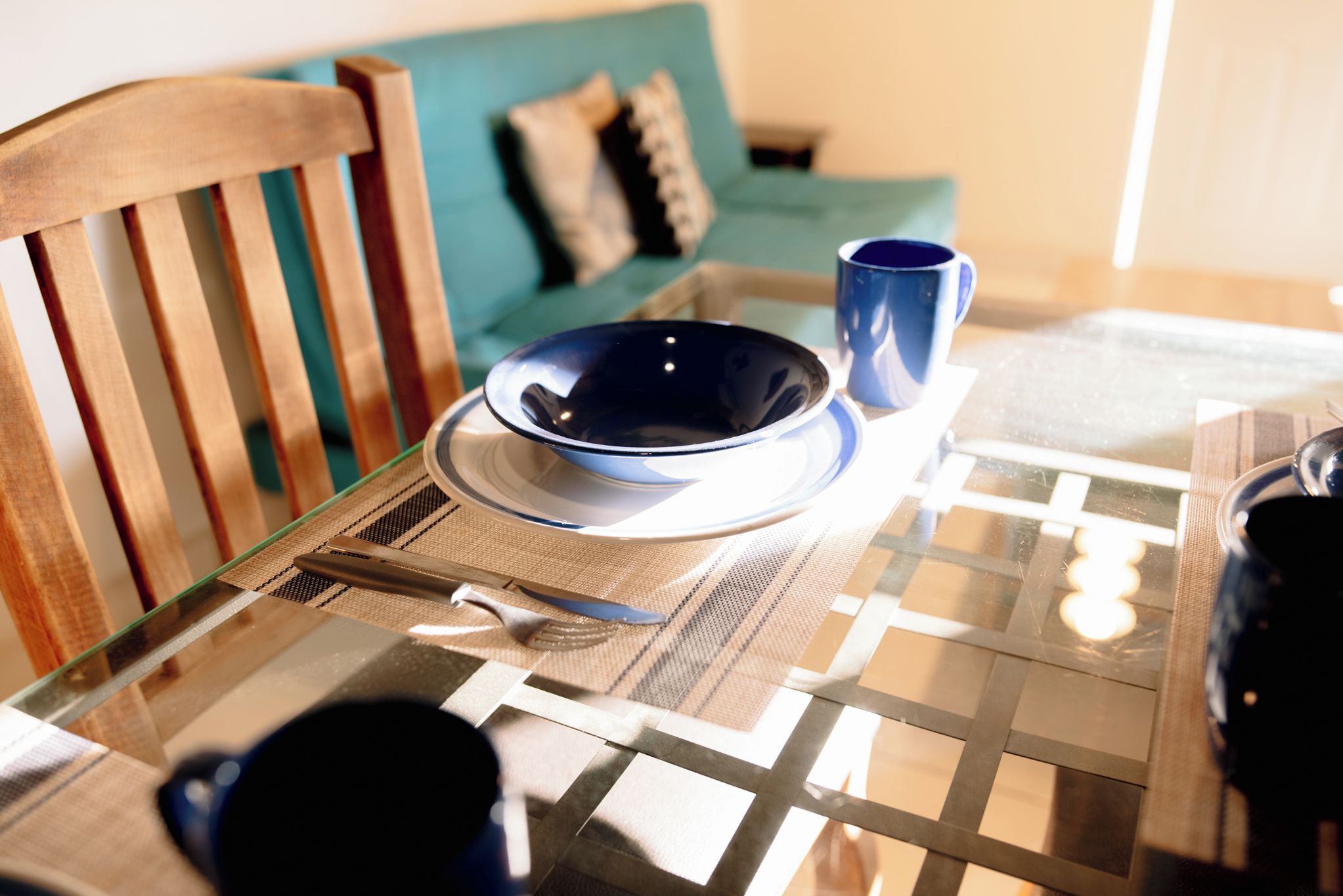 Una mesa de comedor con cubierta de vidrio, un tazón azul, un cuchillo y una taza azul.