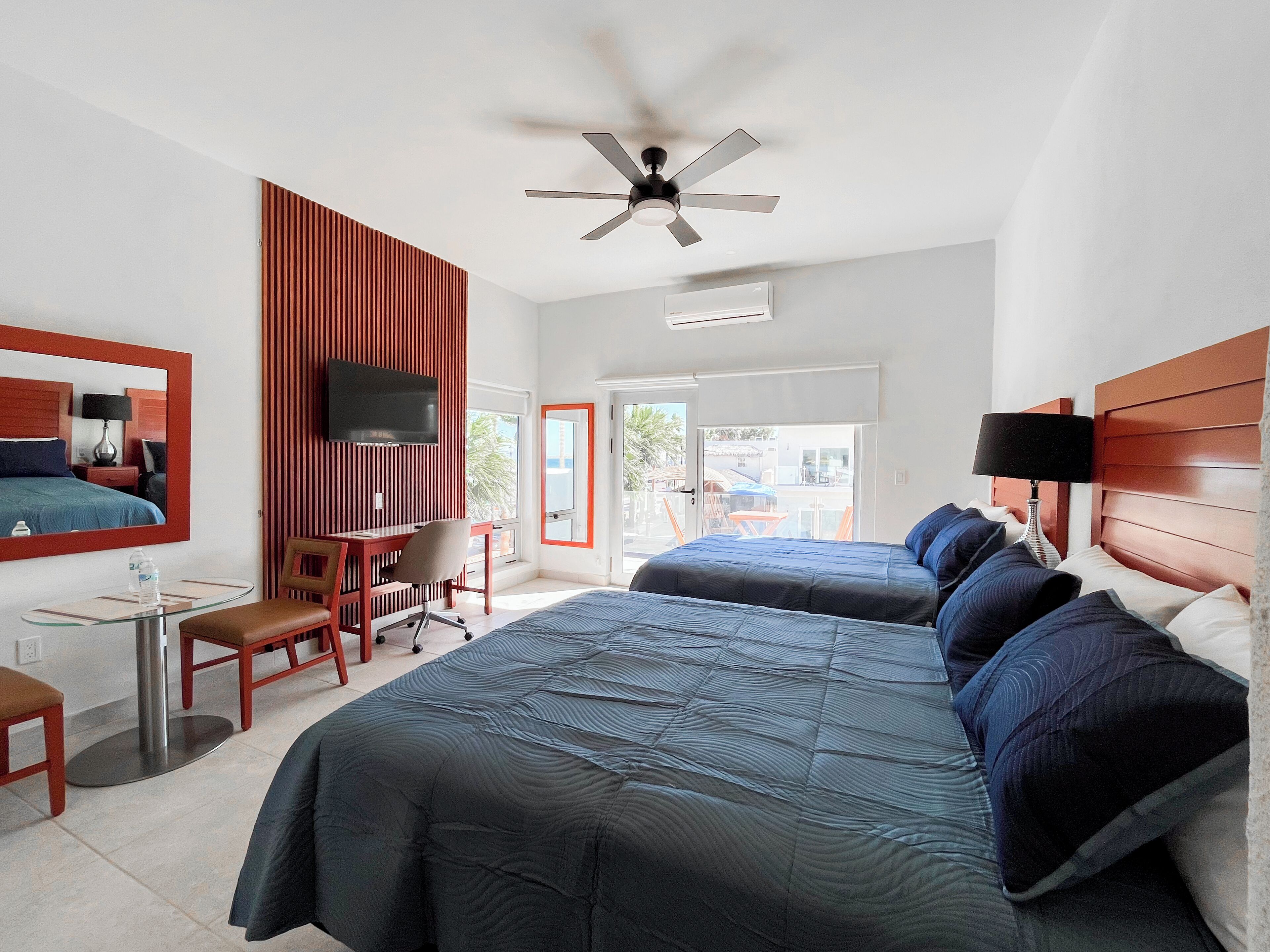 A hotel room with two beds, a desk, a chair, a TV, and a ceiling fan.