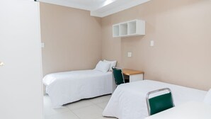 A small, clean room with two single beds, a desk, and a chair. - Glenada Hotel (Johannesburg South)