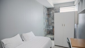 A modern bedroom with a bed, a small table, and a shower area. - Glenada Hotel (Johannesburg South)