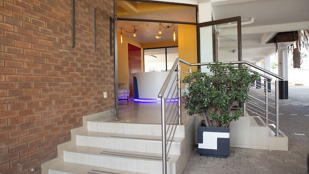 A staircase with metal railings leading to a reception area with a large plant and a blue-lit interior. - Glenada Hotel (Johannesburg South)