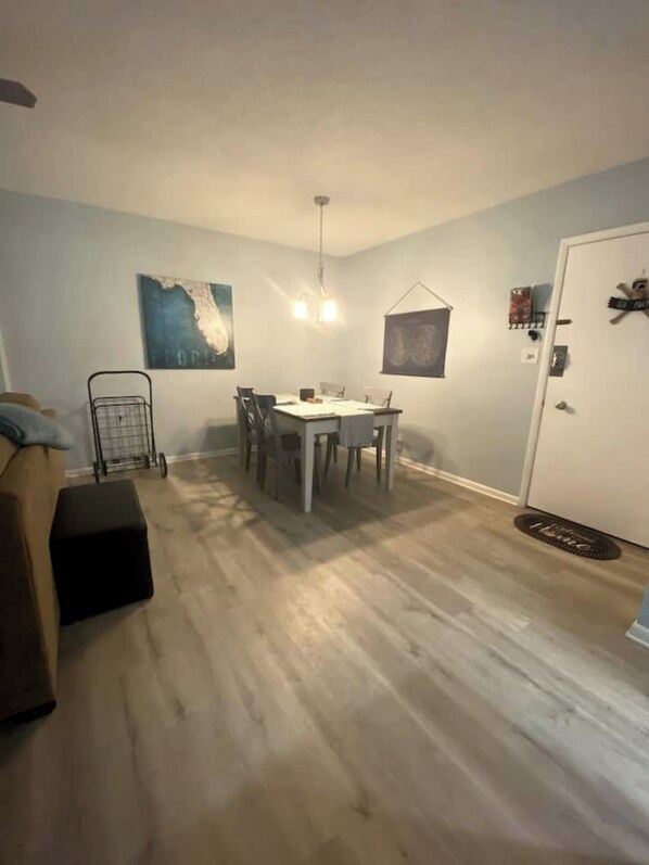 Un comedor con una mesa y sillas, una lámpara colgante y una puerta con felpudo.