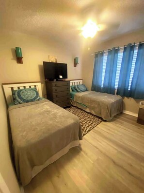 Un dormitorio con dos camas, un aparador, un televisor y una ventana con cortinas.