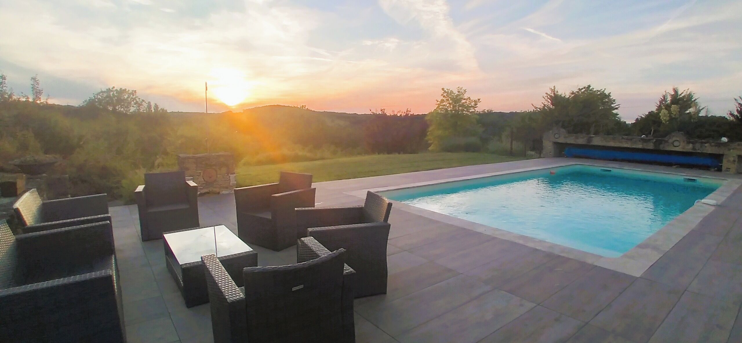 Piscina con zona de terraza, mobiliario exterior y vistas al atardecer.