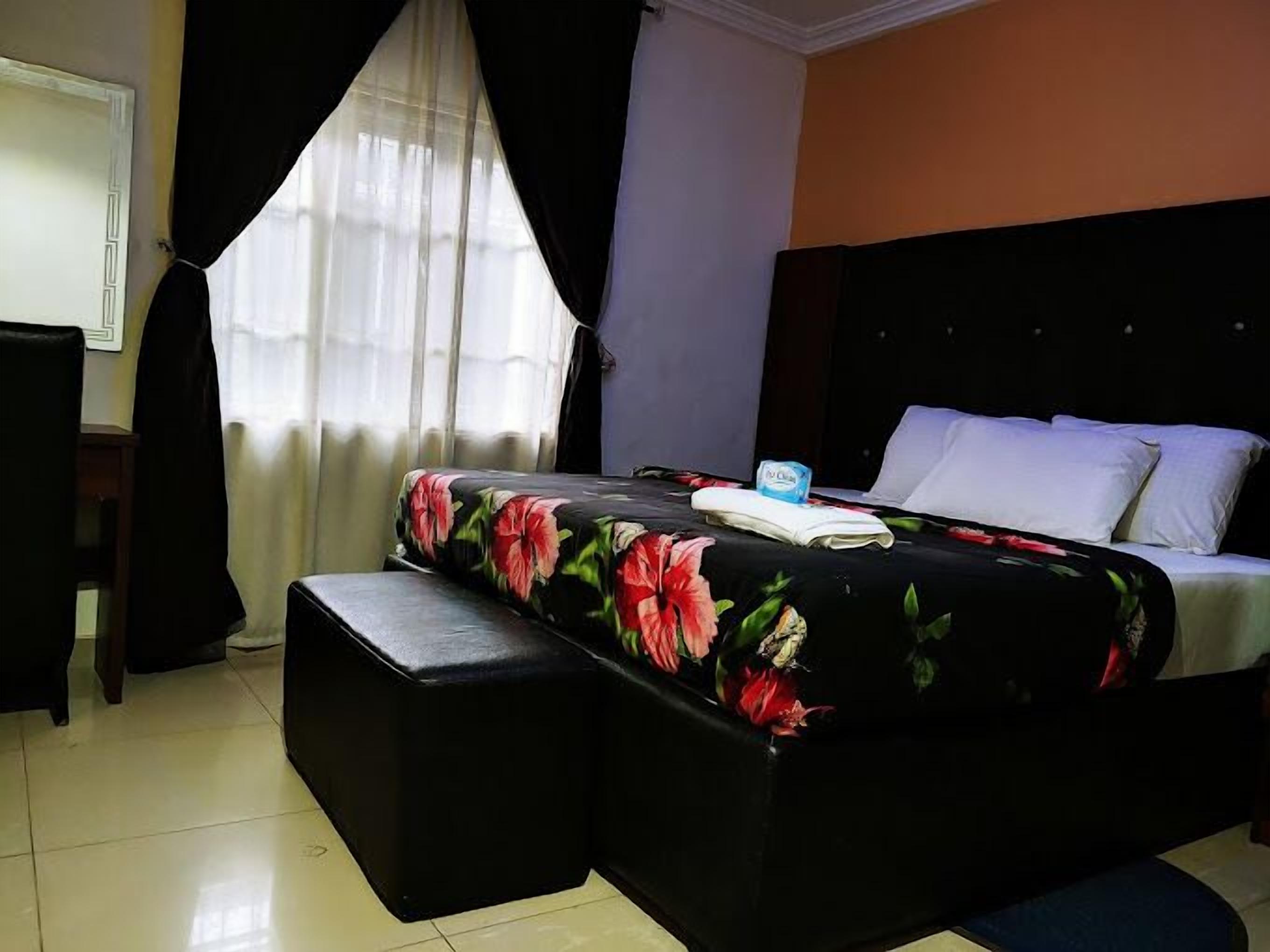 Habitación de hotel con una cama, un banco, un televisor y un ventanal con cortinas.