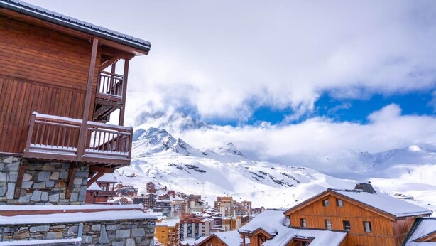A wooden building with a balcony, a stone base, and a snowy mountain backdrop. - 1st floor, swimming pool, sauna, hammam, balcony, fireplace or stove, tv, ski locker, 68m² (Val Thorens)