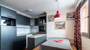 A compact kitchen with modern appliances, a dining area with a table and bench, and a red pendant light. - 1st floor, swimming pool, sauna, hammam, balcony, fireplace or stove, tv, ski locker, 68m² (Val Thorens)