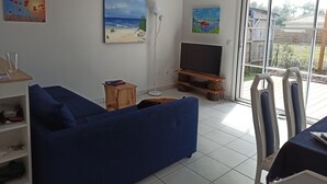 Ein Wohnzimmer mit einem blauen Sofa, einem Fernseher auf einem Holzboden und Kunstwerken an den Wänden.