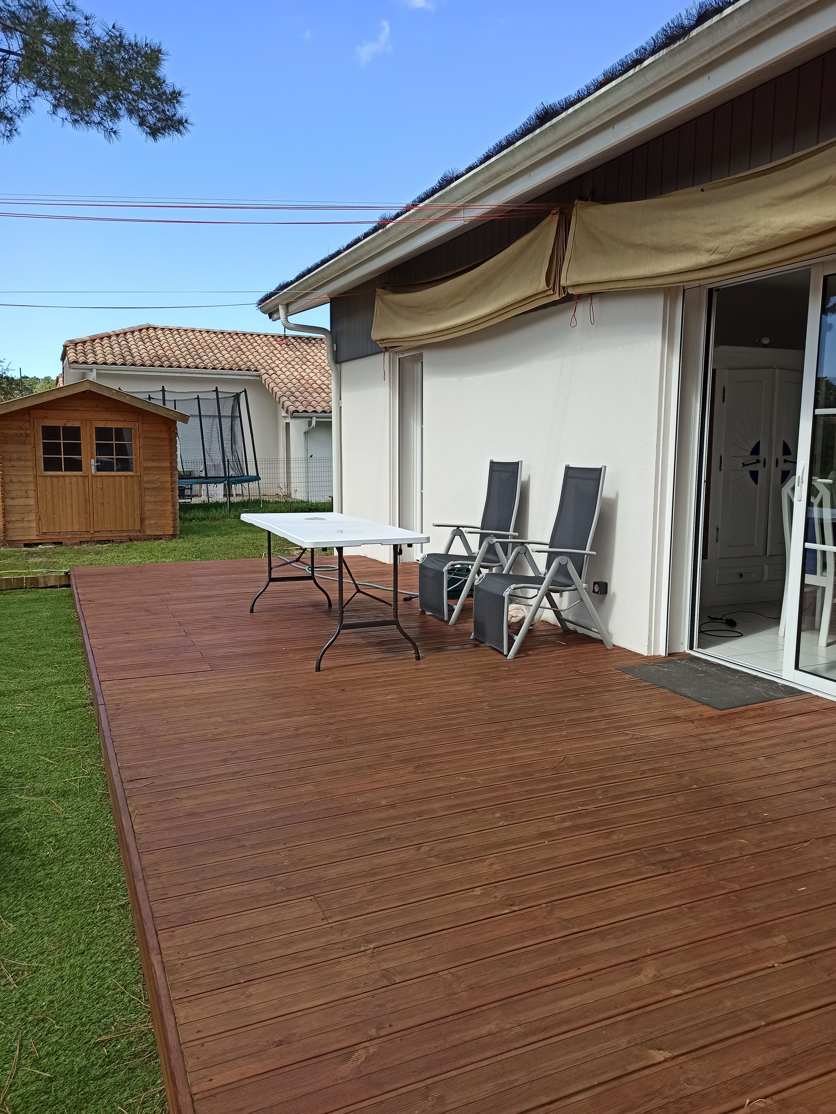 Un terrazzo in legno con tavolo e sedie, un portico coperto e una casa con una porta scorrevole in vetro.
