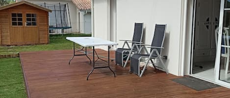 Une terrasse en bois avec une table et des chaises, un patio couvert et une maison dotée d’une porte-fenêtre coulissante.