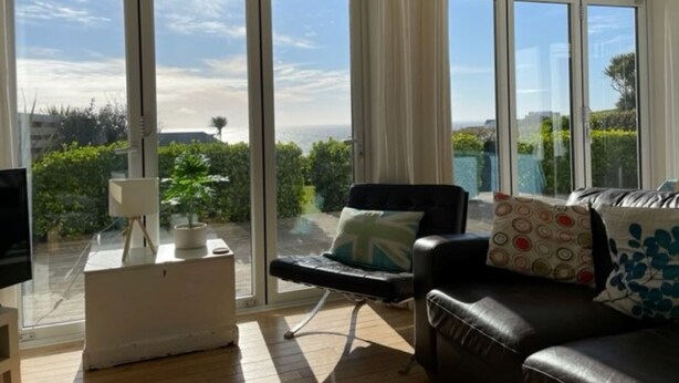 A spacious room with a large sliding glass door leading to a balcony, a black leather sofa, a white side table, and a television.