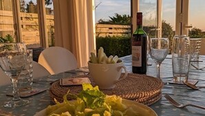 A table set for dining with a bowl of salad, a bottle of wine, and glasses on a table with a view of the outdoors.