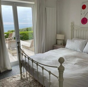 Relax in this serene bedroom with a large bed, a bedside table, and a window offering a view of the outdoor deck.