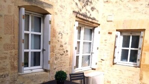 An outdoor patio with a stone floor, a table with chairs, and two windows with shutters. - Bayeux, Appartement Le Clem's'right in the heart of town and tourist sites. (Bayeux)