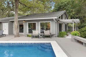Ein Haus mit Pool, Sitzgelegenheiten im Freien und einer Pergola.